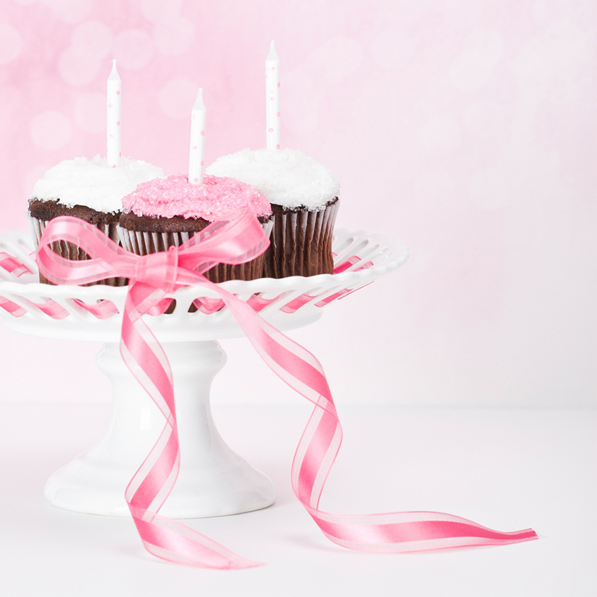 Cupcakes with candles on cake stand with pink ribbon